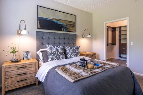 A bedroom with a large bed, a nightstand with a plant, and a painting on the wall.