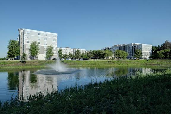 A fountain in the middle of a grassy area in front of apartment buildings.