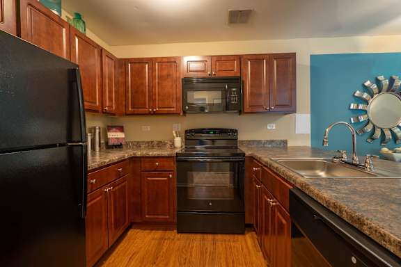 A black refrigerator is in a kitchen with wooden cabinets.