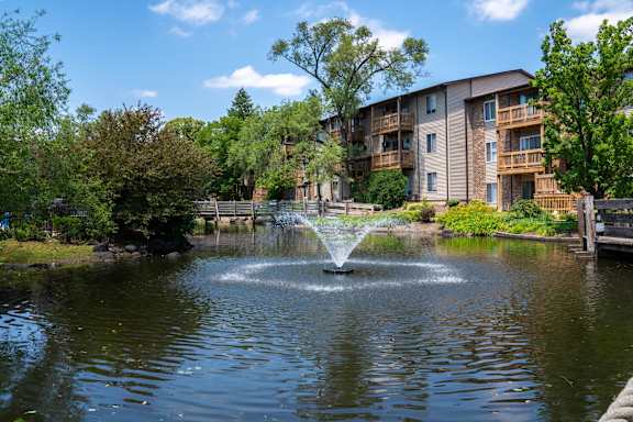 A fountain in the middle of a pond in front of apartment buildings.