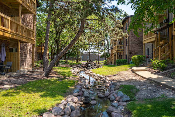 A stream runs through a grassy area between two apartment buildings.