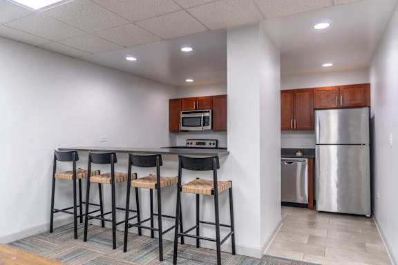 A kitchen with a refrigerator, microwave, oven, and bar stools.