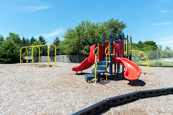 A playground with a red slide and yellow safety bars.