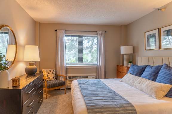 A bedroom with a large bed and a chair by the window.