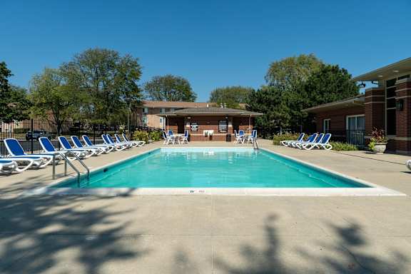 A swimming pool surrounded by chairs and trees.