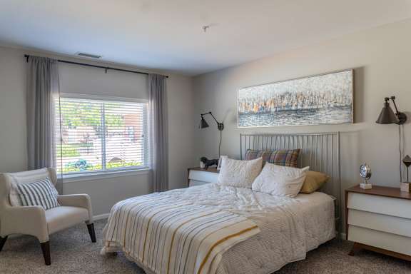A bedroom with a bed, chair, and painting on the wall.