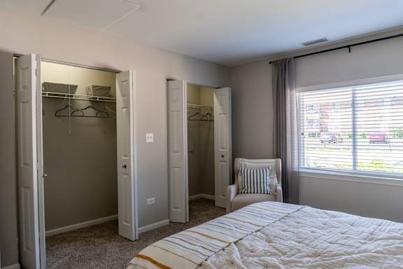 A bedroom with a bed, chair, and three closets.