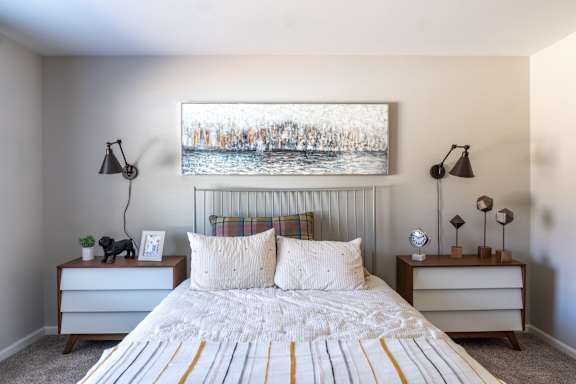 A bedroom with a bed, two nightstands, and a painting on the wall.