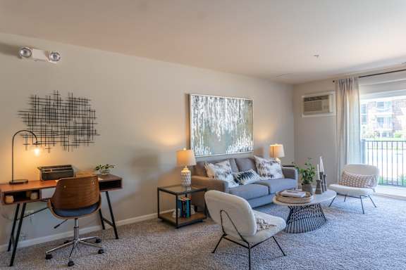 A well-lit living room with a grey sofa, a wooden desk, and a chair.