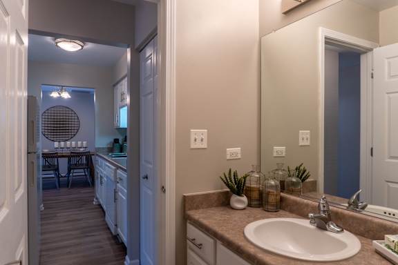 A bathroom with a sink, mirror, and a view of a dining area.