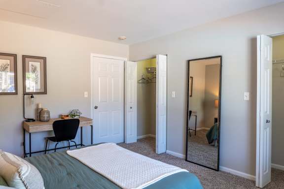 A bedroom with a bed, desk, and mirror.