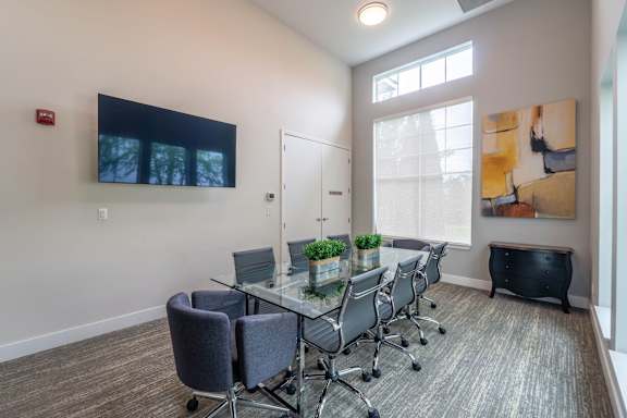 A conference room with a glass table and grey chairs.