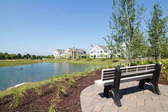 A bench is in the foreground of a residential area with houses and a lake in the background.