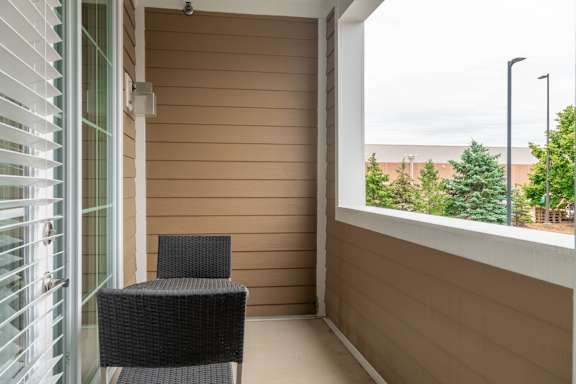 A black chair sits on a balcony with a view of trees and a cloudy sky.