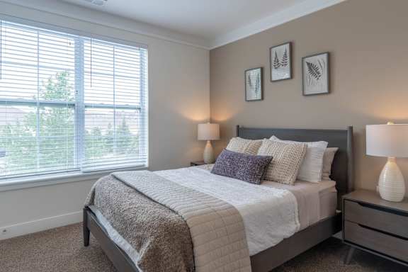 A bedroom with a bed, two lamps, and a window with blinds.