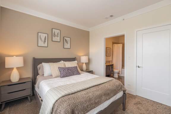 A bedroom with a large bed, two lamps, and a carpeted floor.