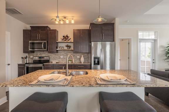 A kitchen with granite countertops and dark brown cabinets.