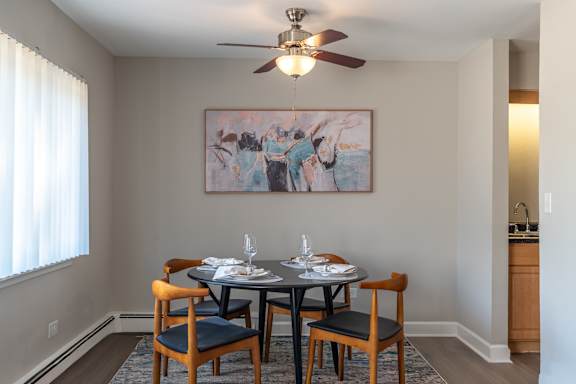 A dining room with a table set for two and a painting on the wall.