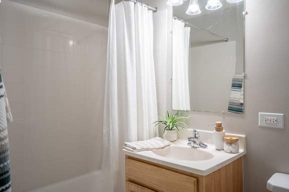 A bathroom with a white shower curtain, a wooden vanity, and a mirror.
