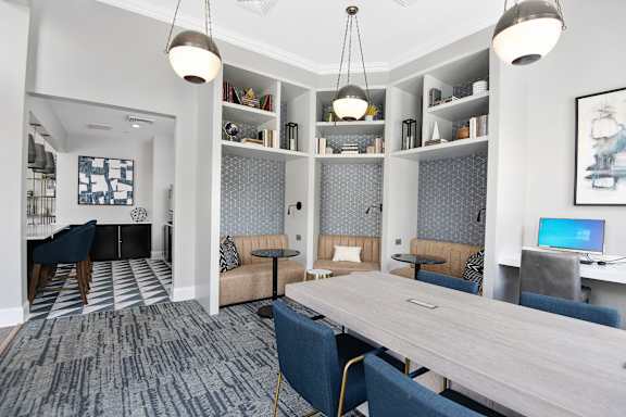 A modern office space with a long table, chairs, and a laptop on a desk.