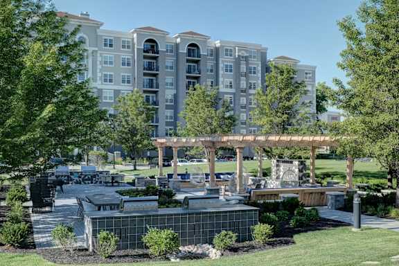 A large building with a lot of windows is behind a landscaped area with a fountain.
