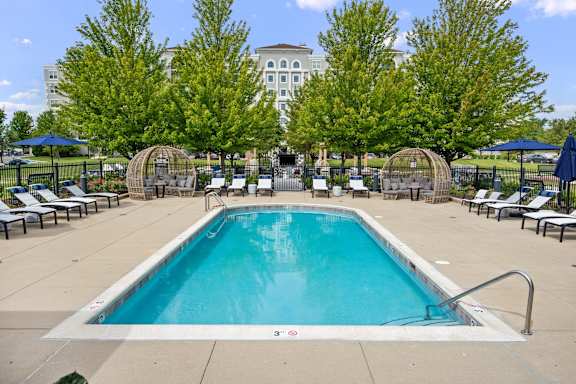 A large swimming pool surrounded by trees and lounge chairs.