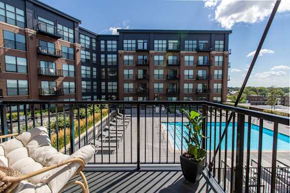 A balcony with a chair and a potted plant overlooks a pool and buildings.