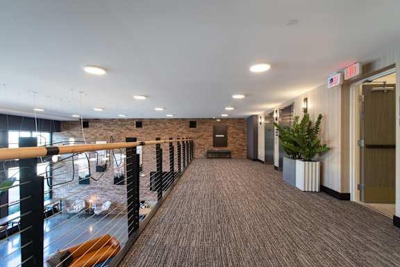 A long hallway with a balcony on the left side and a plant on the right side.