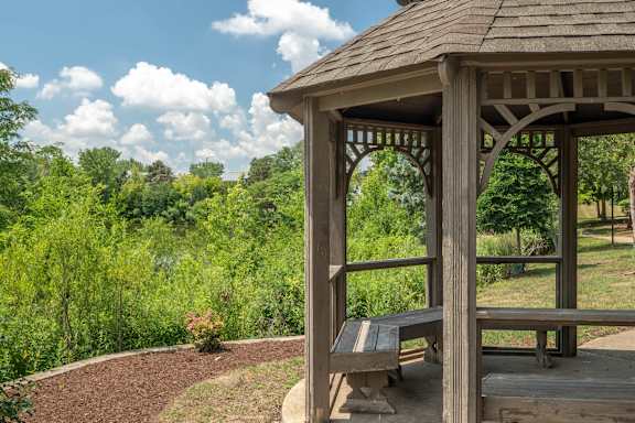 A wooden gazebo with a bench is situated in a garden.