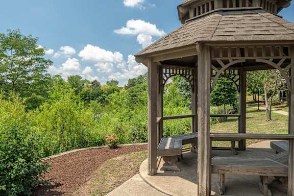 A gazebo with a wooden bench sits in a park.