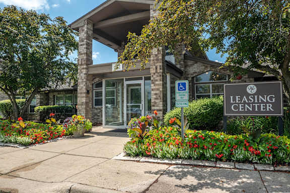 A leasing center is surrounded by flowers and has a handicap parking sign.