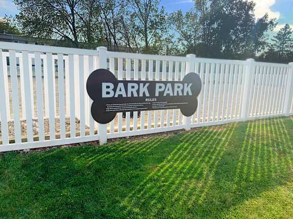 A sign that says Bark Park rules stands in front of a white fence.