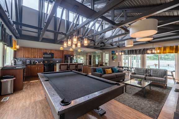 A pool table is in the middle of a room with a kitchen in the background.
