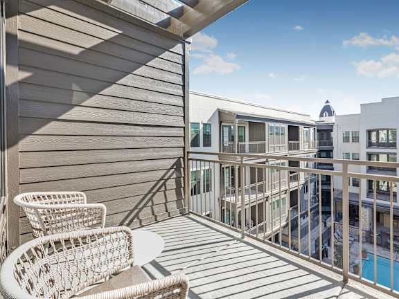 A balcony with a chair and table overlooking a pool.