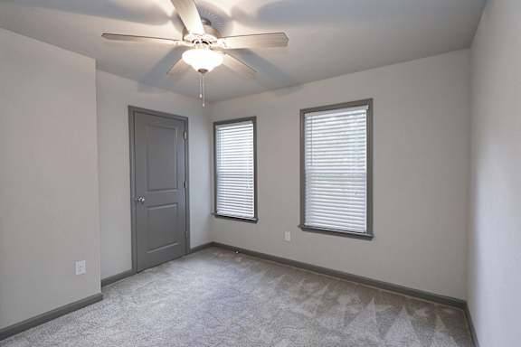 A room with a ceiling fan, a door, and a window with blinds.