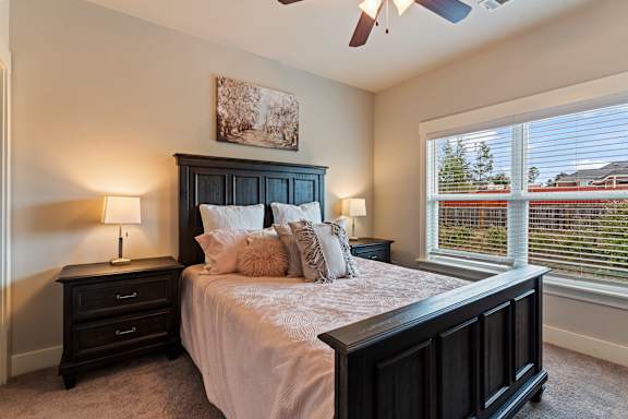 A bedroom with a large bed, a ceiling fan, and a window with blinds.