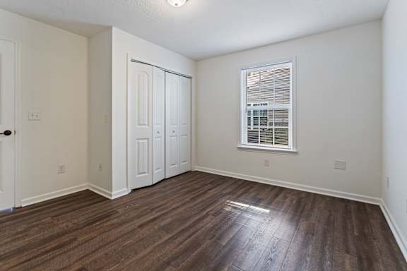 A room with wood flooring and a window with blinds.