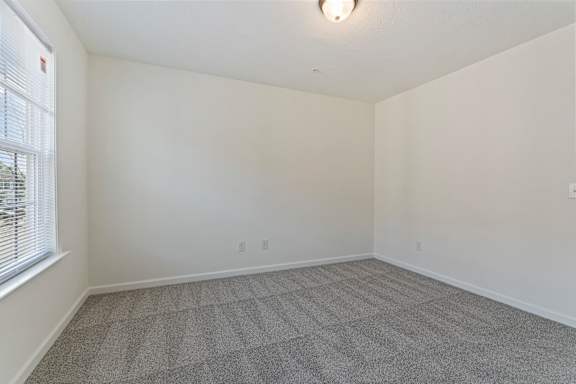 A room with a carpeted floor and a window with blinds.