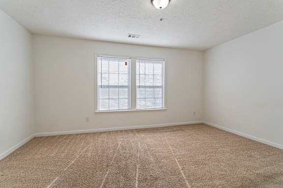 A room with a carpeted floor and a window with blinds.