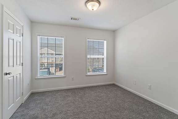 A room with a carpeted floor, two windows, and a door.