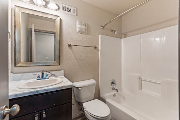 A bathroom with a white tub, sink, toilet and mirror.