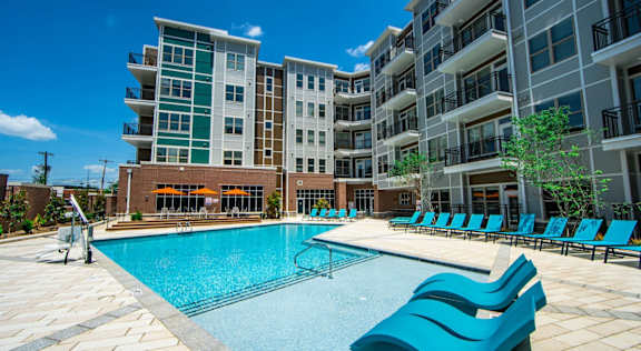 A large swimming pool with blue lounge chairs in front of apartment buildings at The Collective NoDa, Charlotte