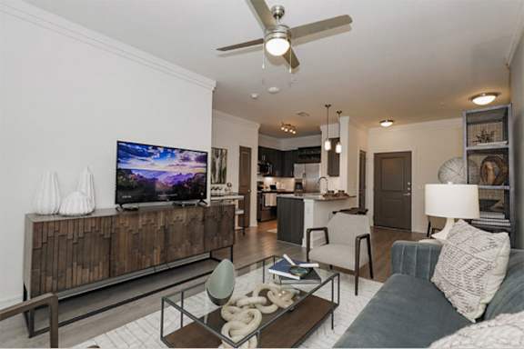 A modern living room with a flat screen TV and a ceiling fan at Cue Luxury Apartments, Cypress, Texas