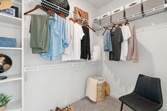 a closet with clothes hanging on a rack and a chair