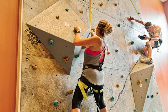 a woman climbing a rock wall with a man on a climbing rope