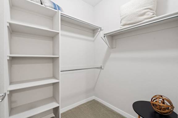 a walk in closet with white walls and shelves and a black stool