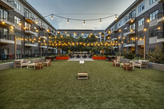 an outdoor lounge area with a firepit and string lights in an apartment complex