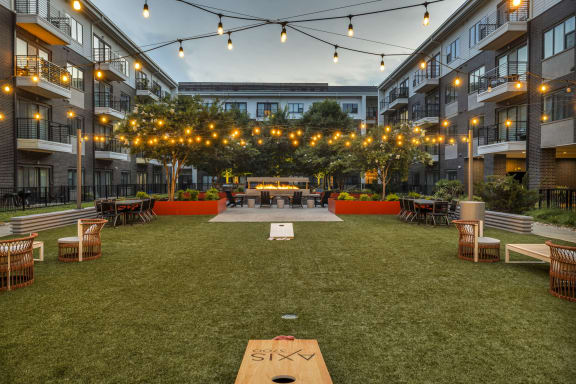 an outdoor lounge area with a shuffleboard table and string lights in an apartment complex