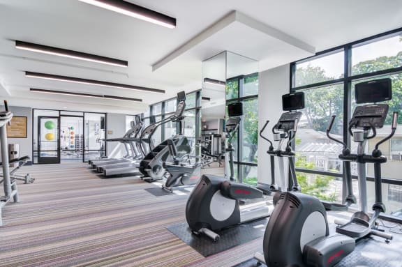 a gym with cardio equipment and large windows