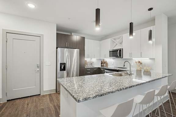 A modern kitchen with a granite countertop and white chairs.